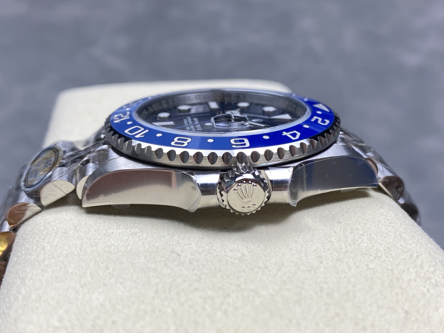 Seitenprofil der hochwertigen Rolex GMT-Master II Replik mit poliertem Edelstahlgehäuse, fluted Krone und Oyster-Armband auf cremefarbenem Kissen