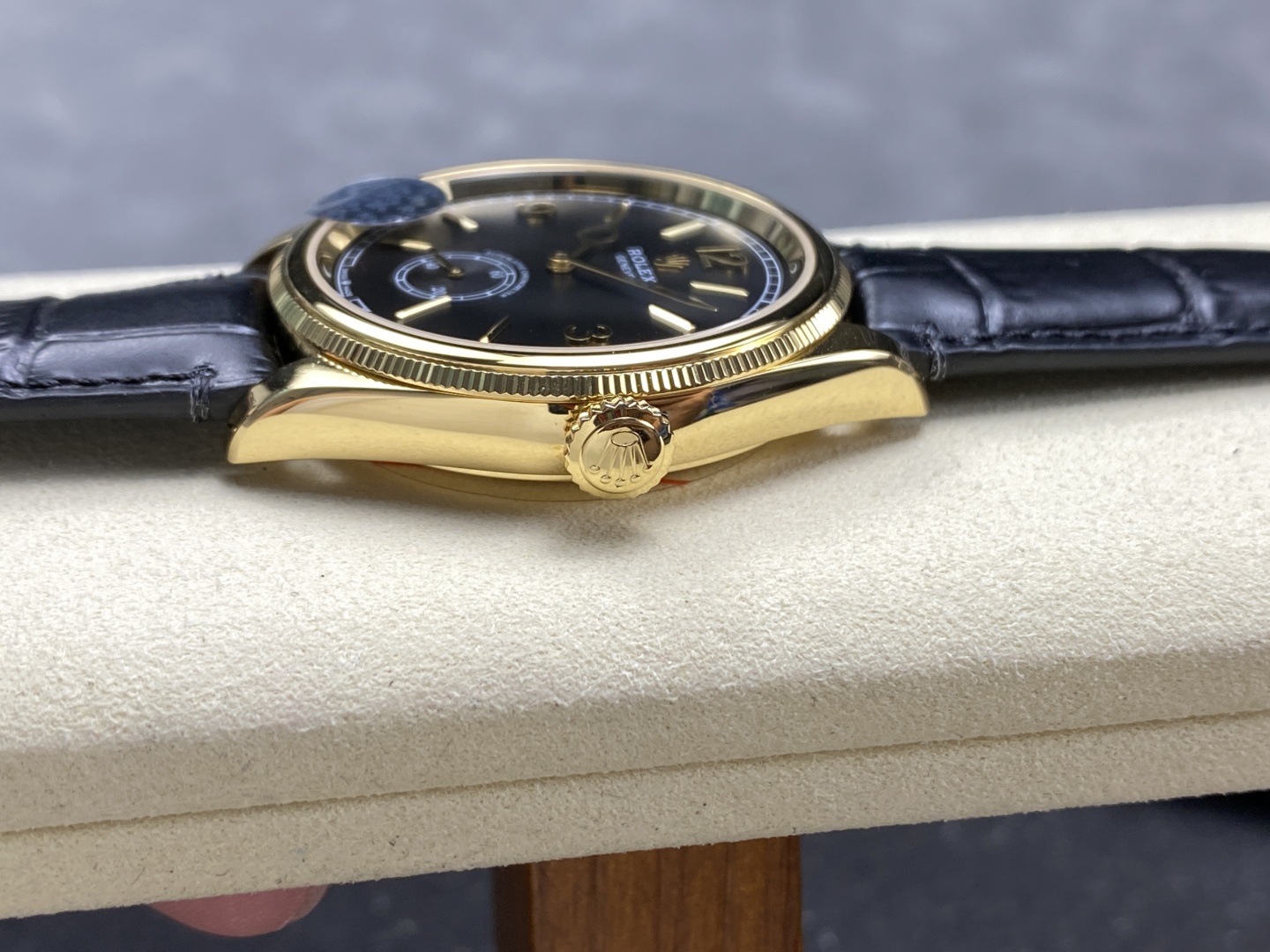 Side profile of a gold Rolex replica watch showing fluted bezel, crown, and black leather strap