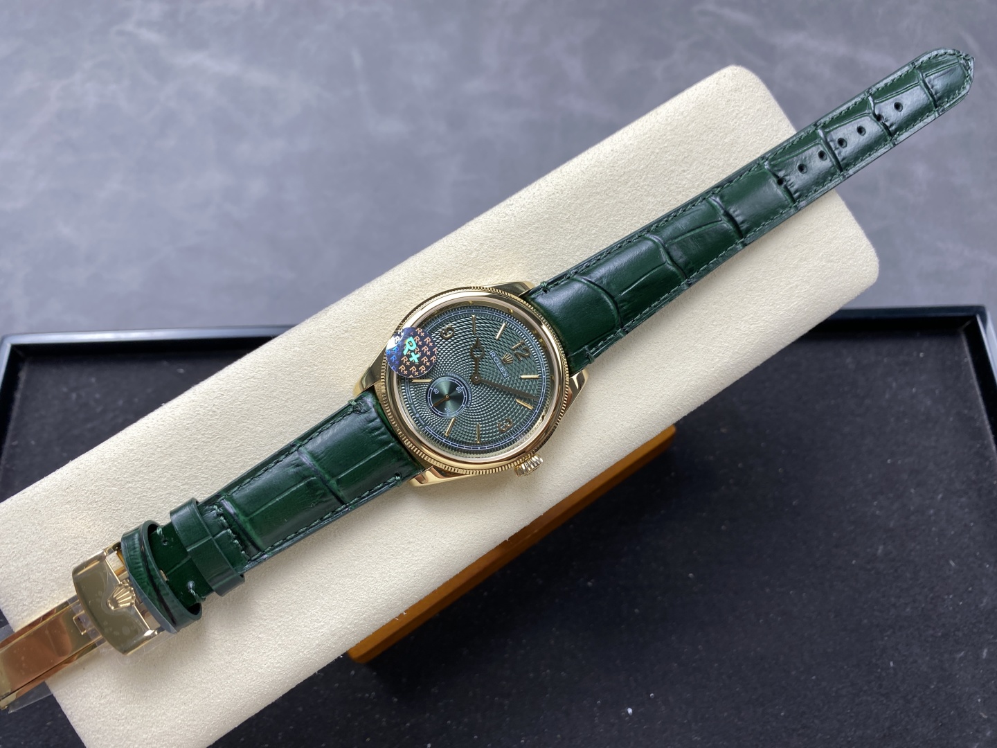 Premium gold Rolex replica with deep green guilloche dial, fluted bezel, and dark green alligator strap displayed on cream cushion