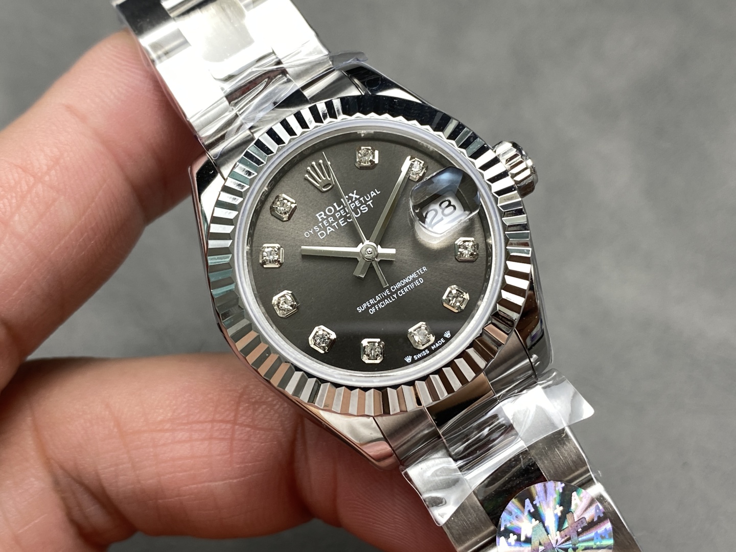 Detailed close-up of the Rolex replica dial with date at 28 under Cyclops lens, diamond markers in square settings, silver hands, and part of the fluted bezel visible