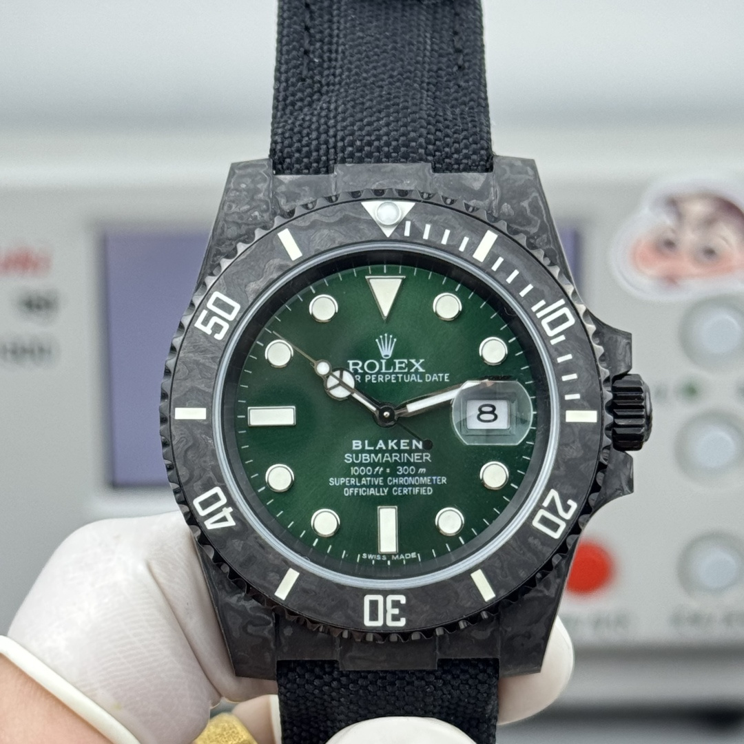 Angled close-up of carbon fiber Submariner replica watch with deep green dial, BLAKEN SUBMARINER branding, luminous triangle at 12, cyclops date lens showing 8, and black fabric NATO strap