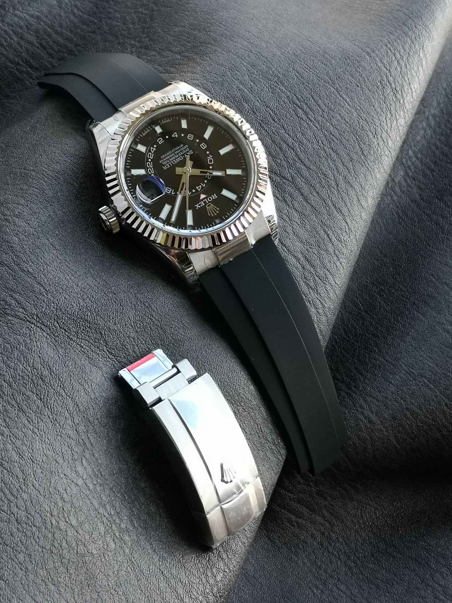 Full watch resting on dark leather surface, showing the clasp and strap integration