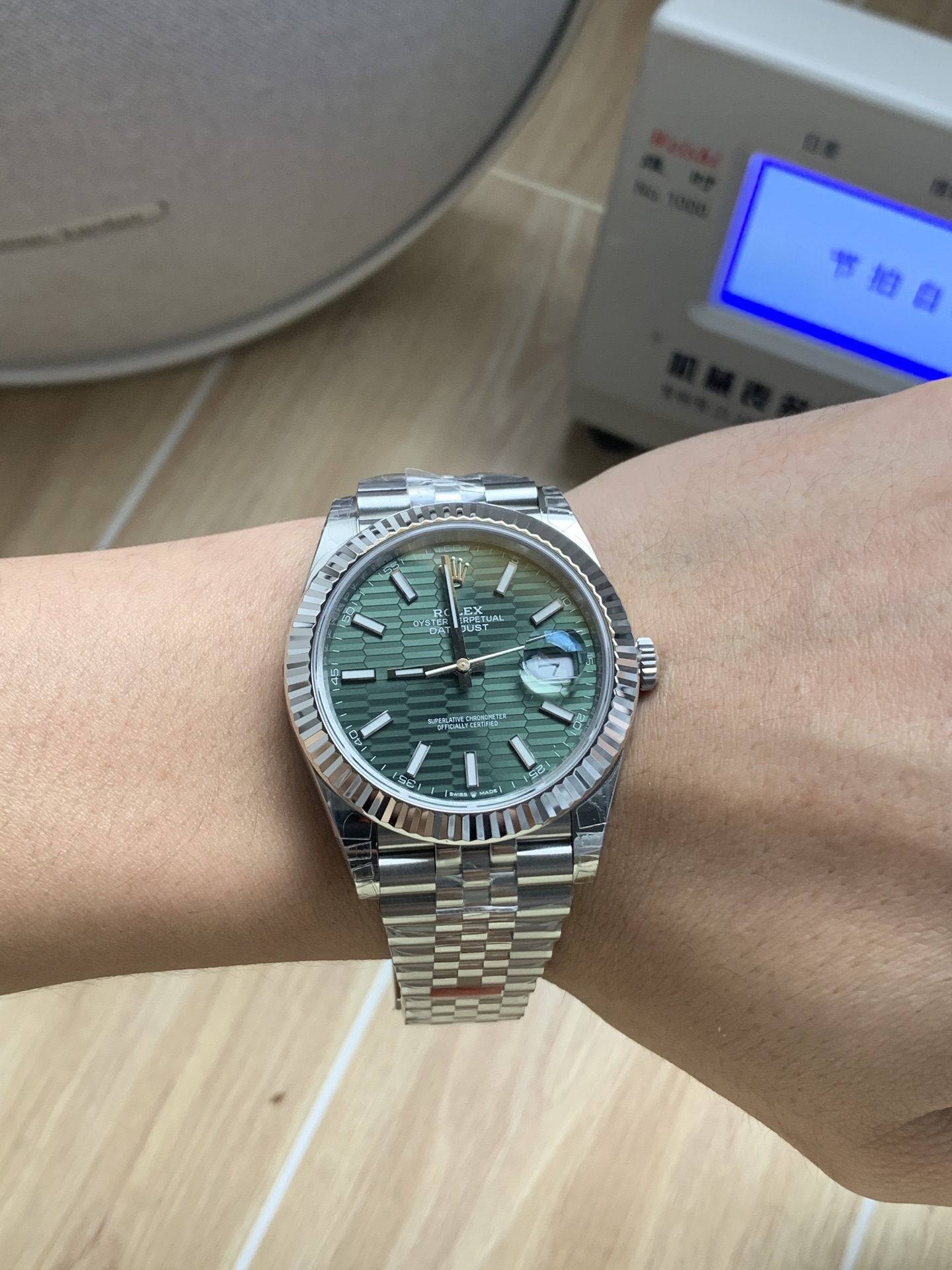 Green dial Rolex Datejust replica on a wrist, showing the fluted bezel and jubilee bracelet in natural light