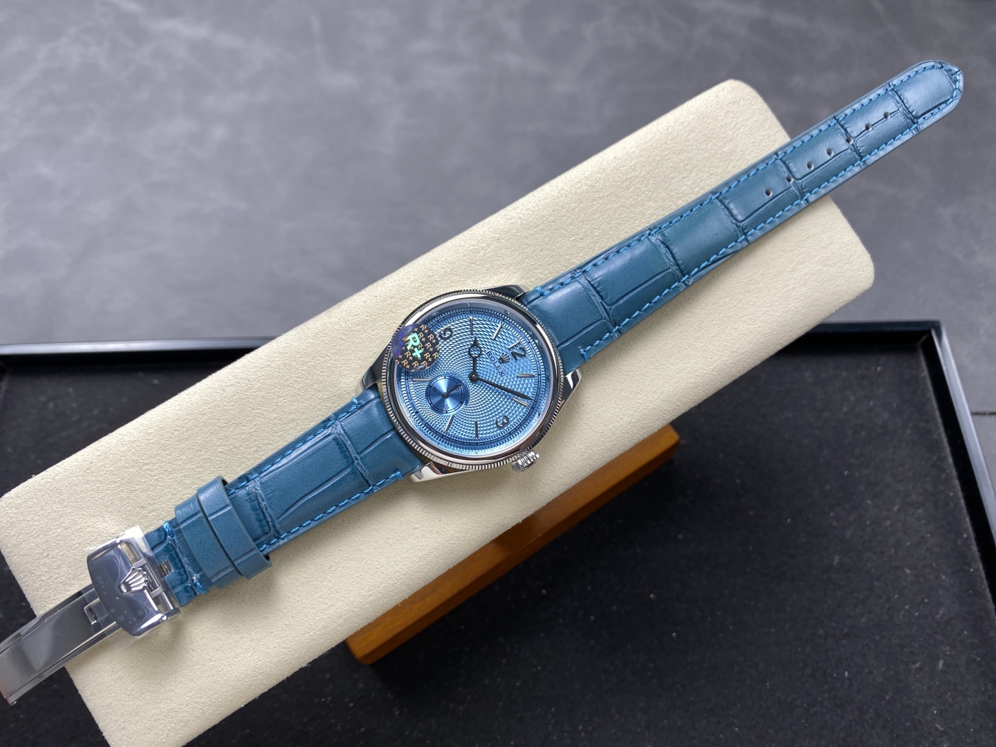 High-quality replica watch with blue dial and sunburst finish displayed on a cream cushion