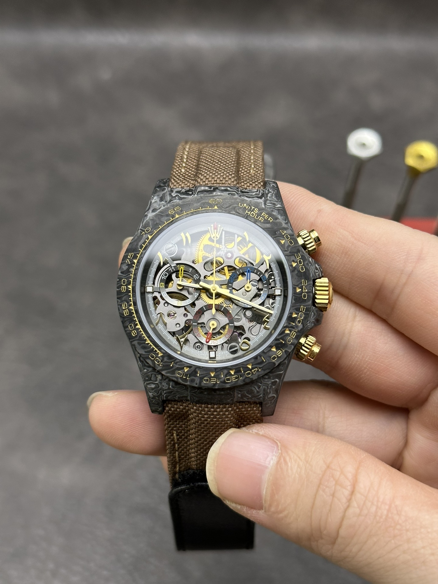 Carbon fiber forged case Daytona with brown strap and gold pushers, 4130 clone movement visible through openworked dial.