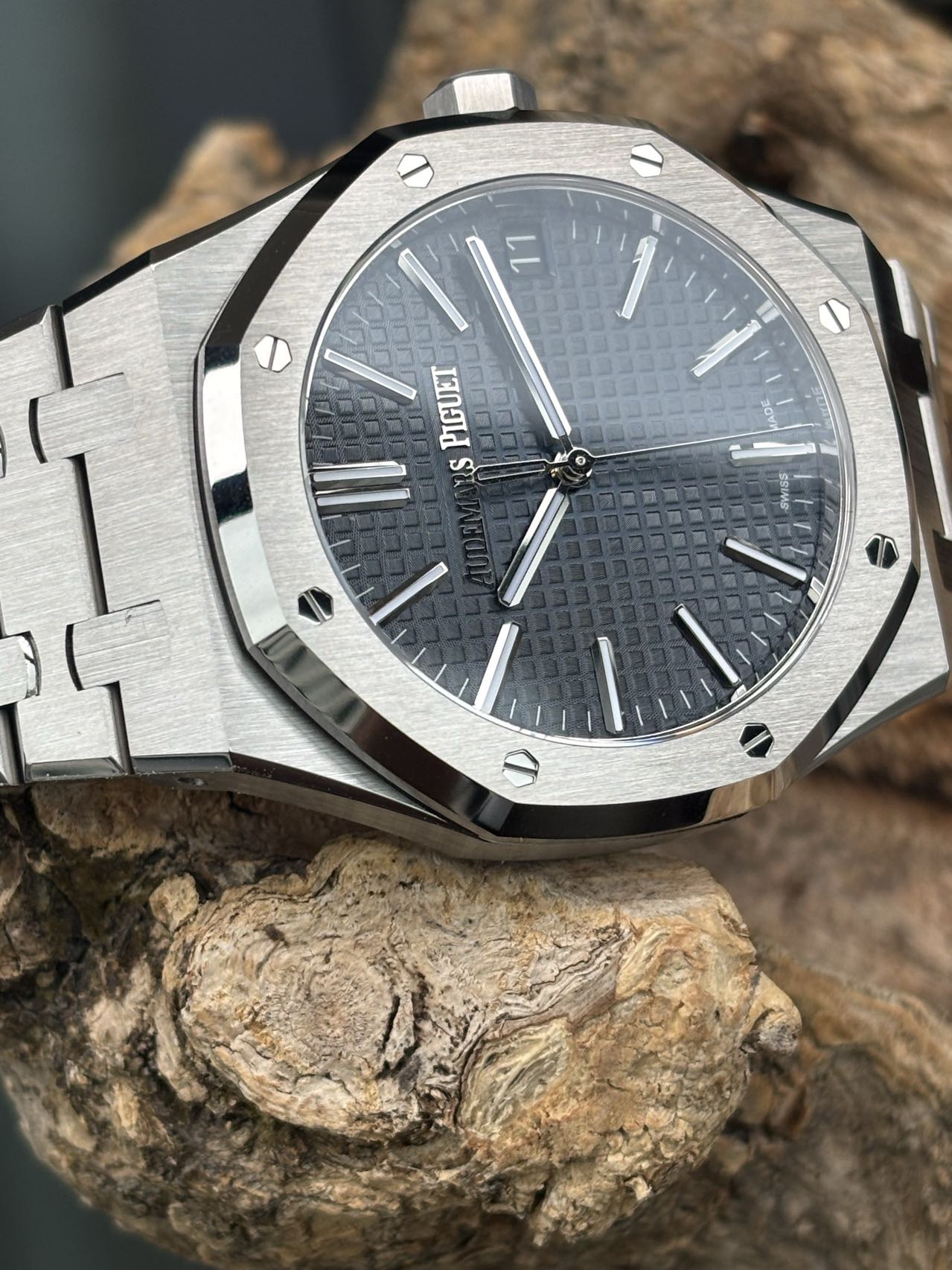 Royal Oak style Audemars Piguet replica watch on wood showing grey Tapisserie dial and brushed bezel