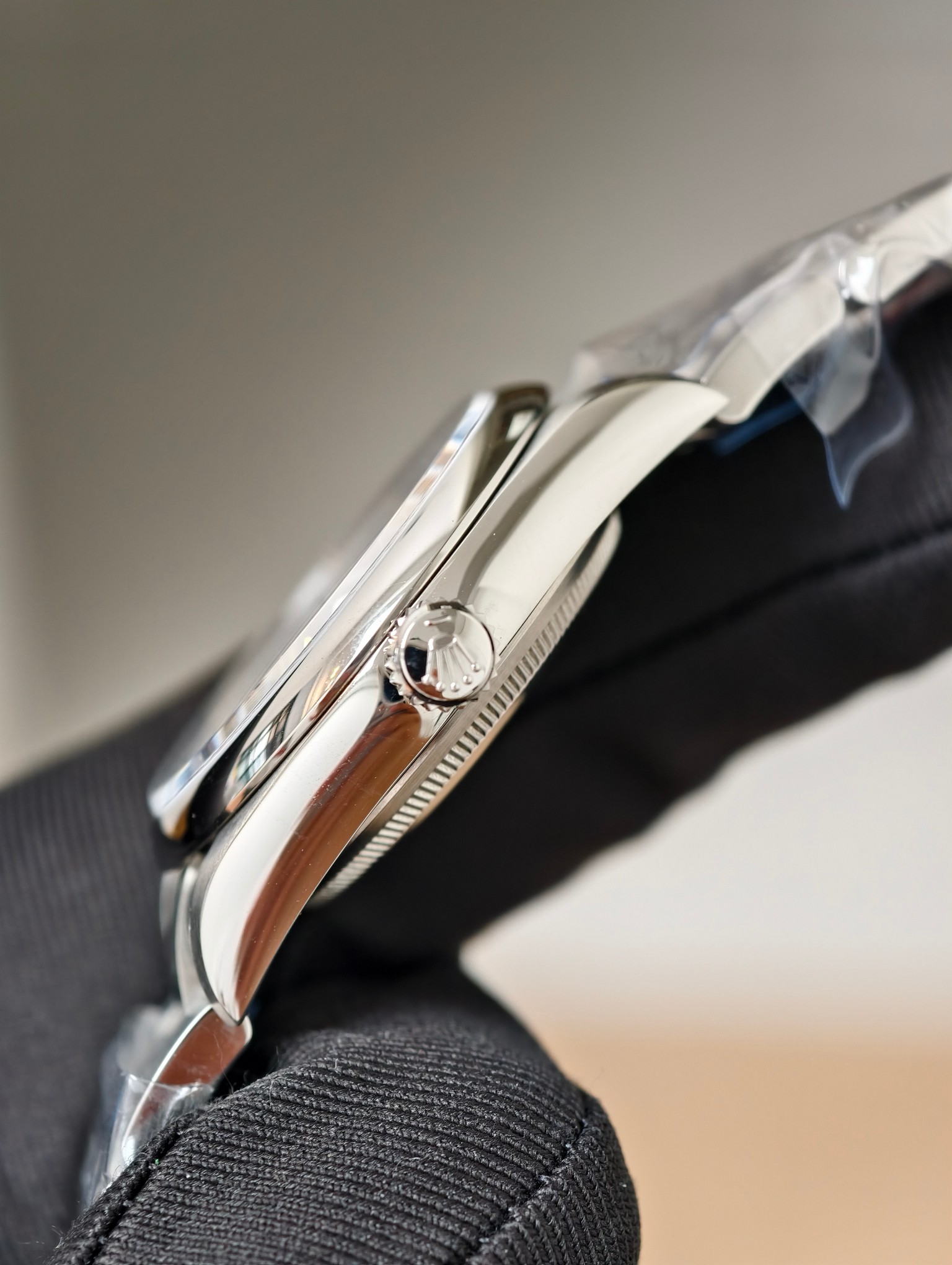 Side-angle close-up of Rolex Oyster Perpetual fluted screw-down crown with engraved logo, polished case, and gloved hand