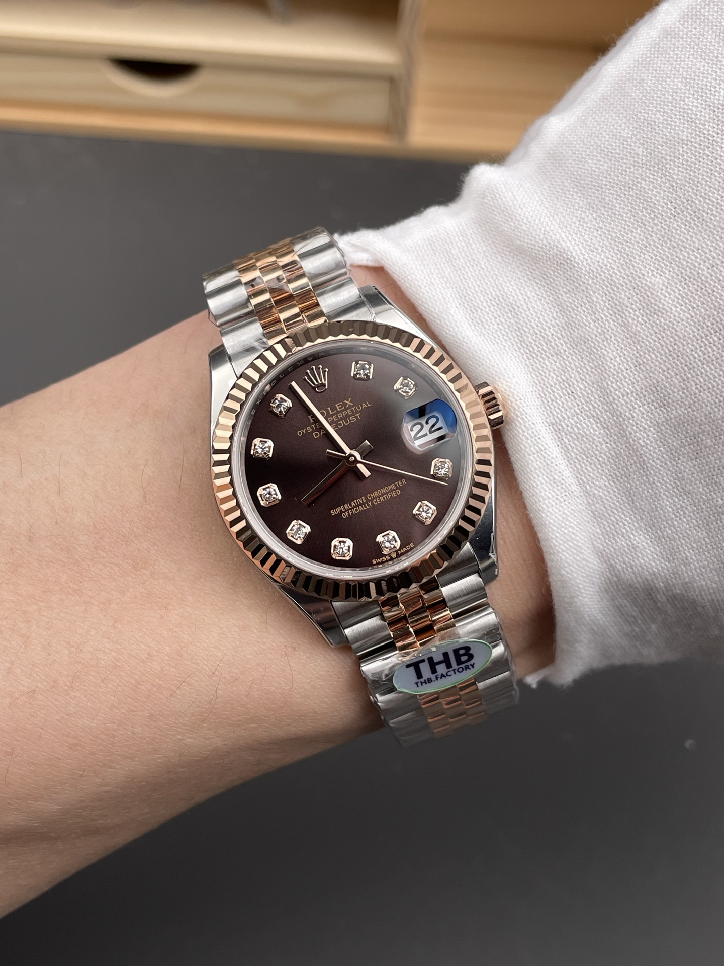 Two-tone Rolex Datejust replica with brown dial diamond markers worn on left wrist under white shirt sleeve