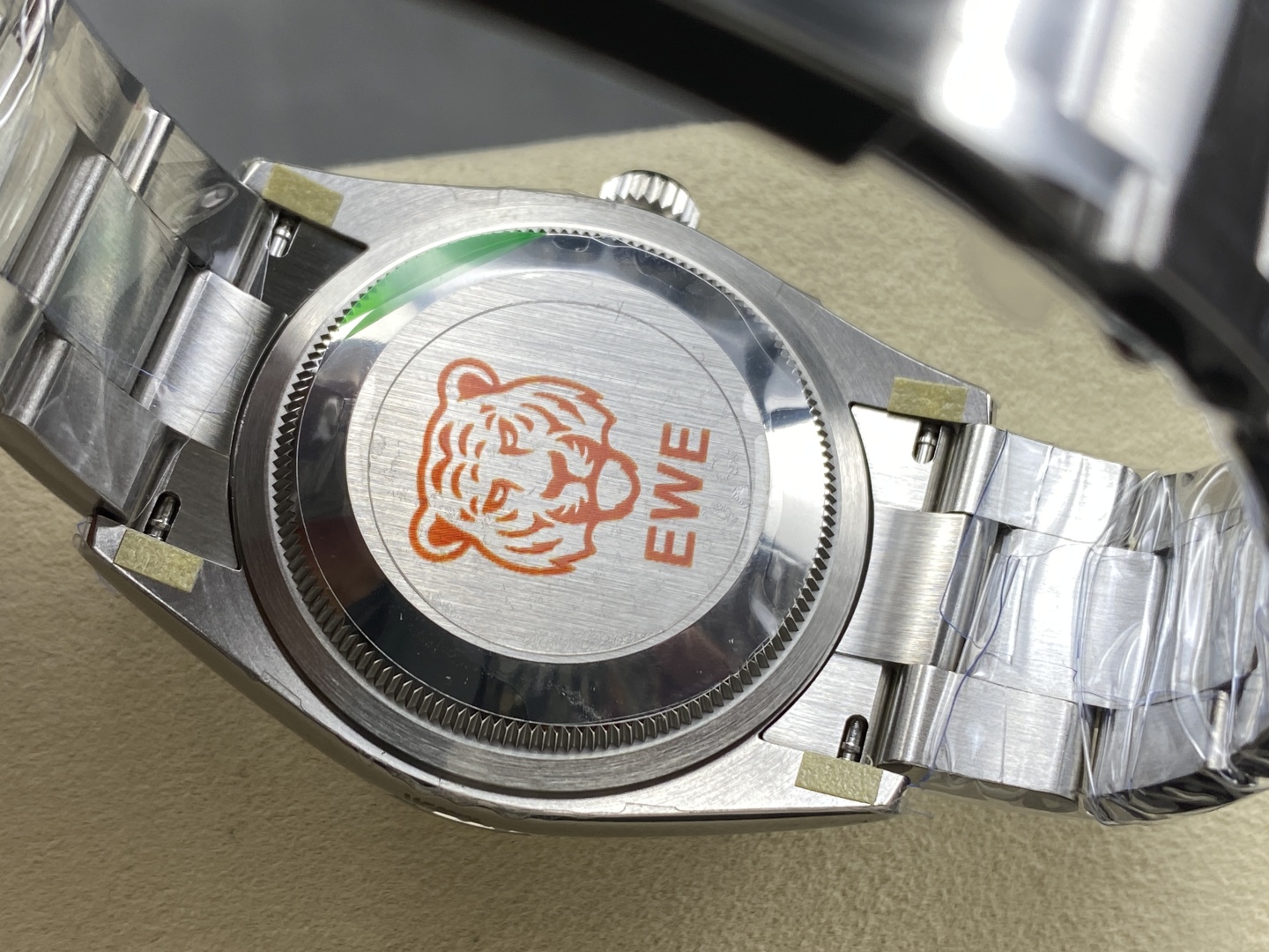 Rear caseback view of the EWE FACTORY replica Rolex watch showing the signature tiger logo and brushed stainless steel construction with protective films