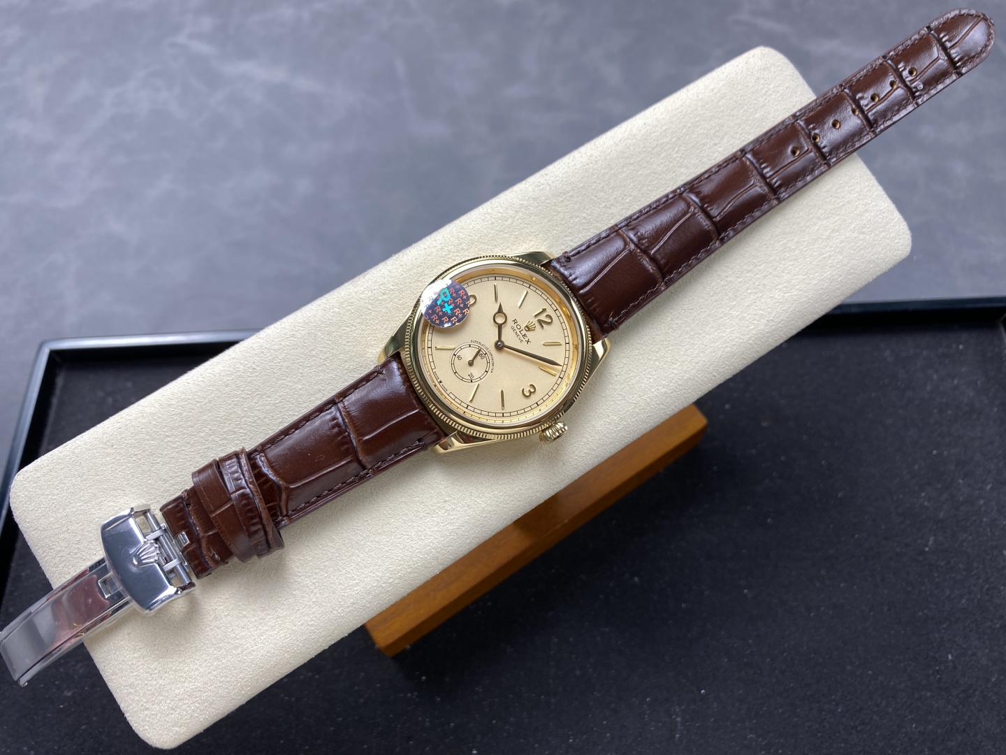Rolex 1908 Clone mit champagnerfarbenem Zifferblatt, braunem Lederband und goldfarbenem Gehäuse auf heller Uhrenrolle