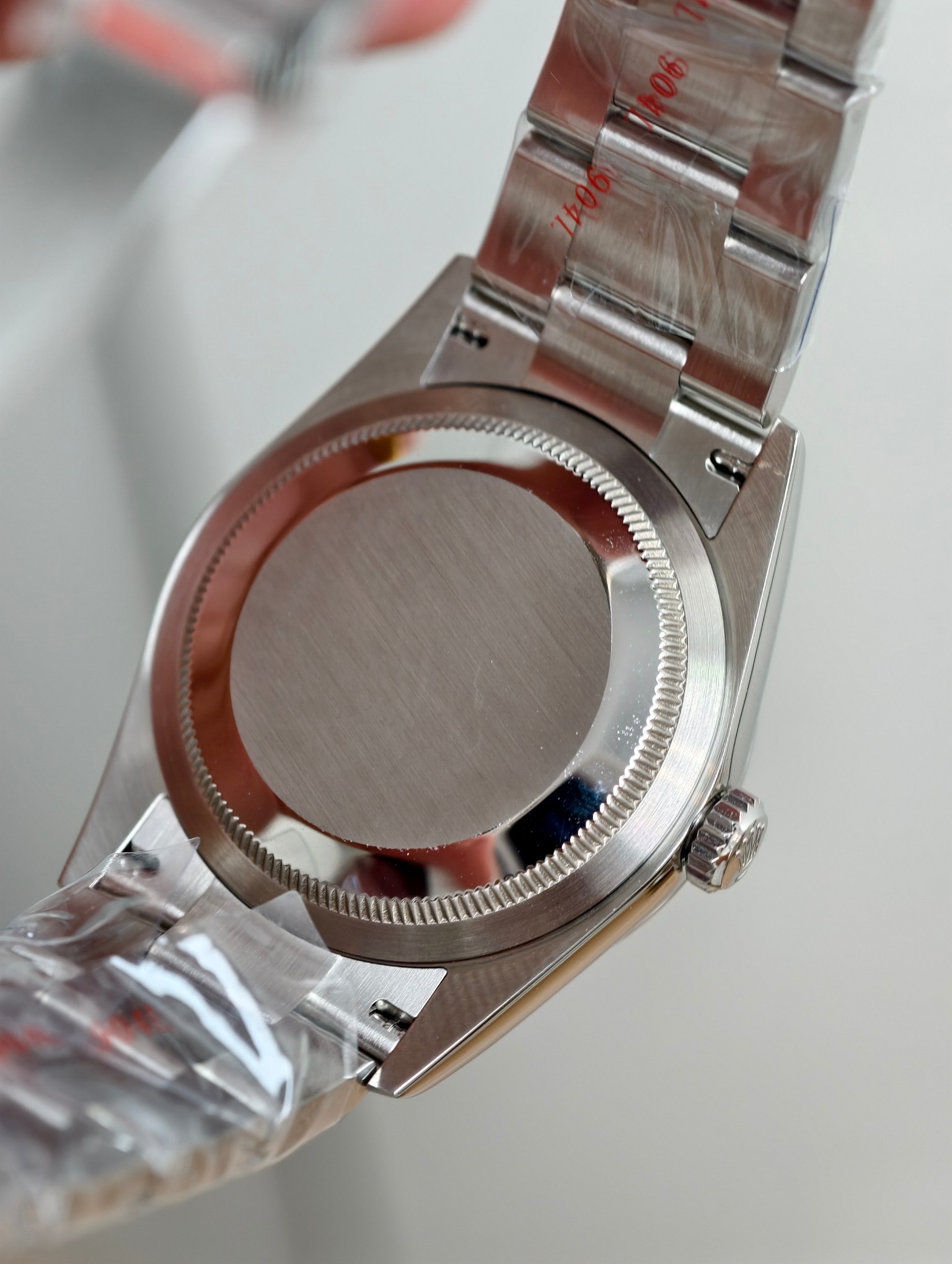 Rear view of Rolex Oyster Perpetual stainless steel caseback with brushed center, fluted edge, and bracelet with 904L marking and protective film