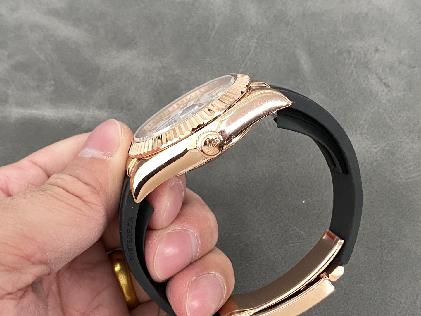 Side view of rose gold Rolex Sky-Dweller replica with fluted bezel and black Oysterflex strap