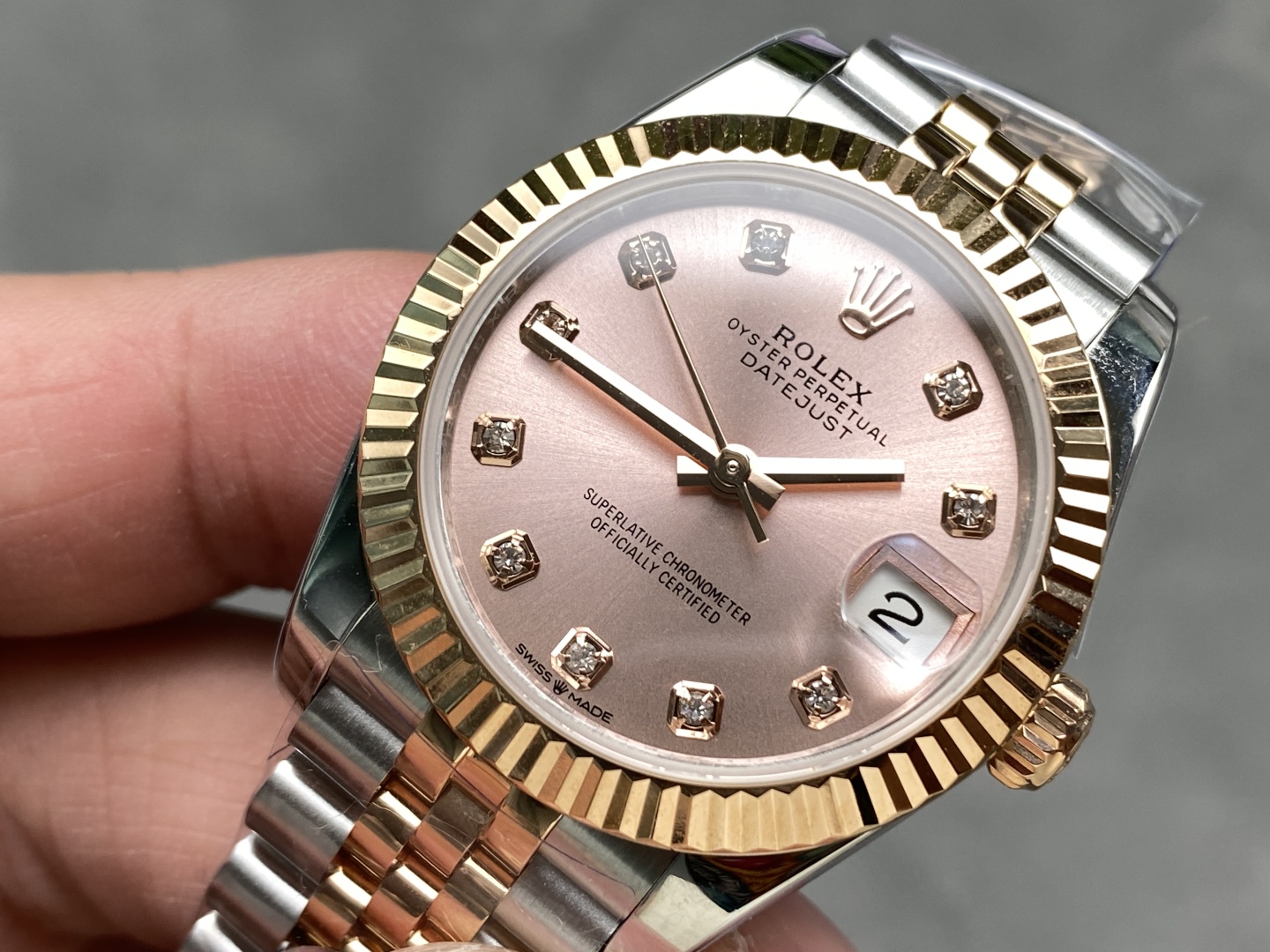 Primer plano de un Rolex falso de dos tonos con esfera rosa, índices de diamantes y bisel estriado dorado.