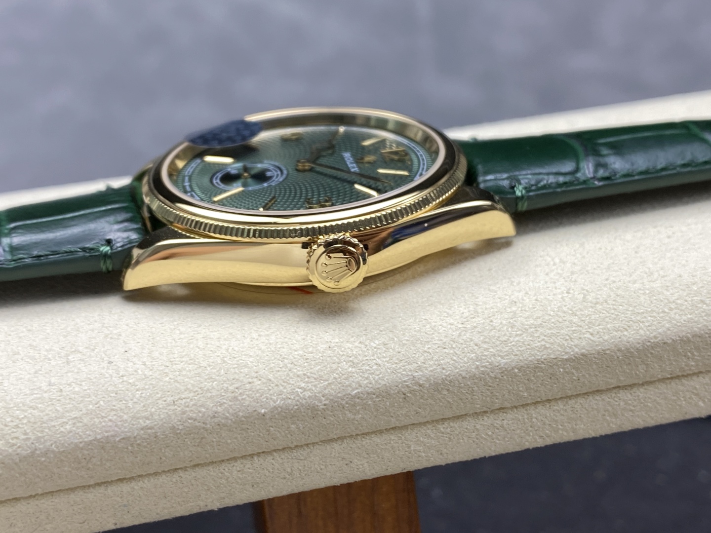 Side angle view of elegant gold Rolex replica watch highlighting the fluted bezel, textured crown and green sunburst dial