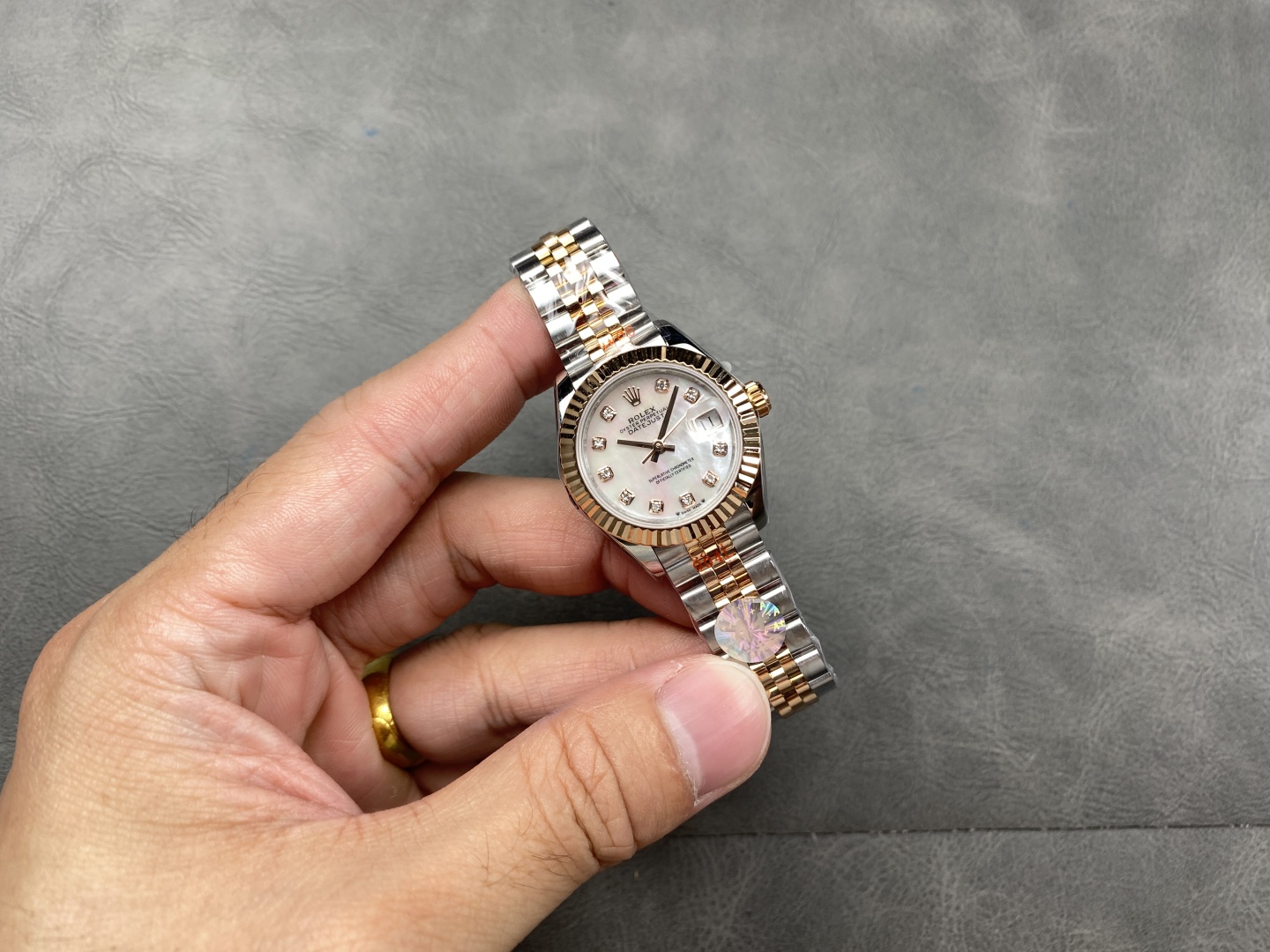 Hand holding an elegant two-tone Rolex Datejust replica with white mother-of-pearl dial, diamond hour markers, and rose gold fluted bezel