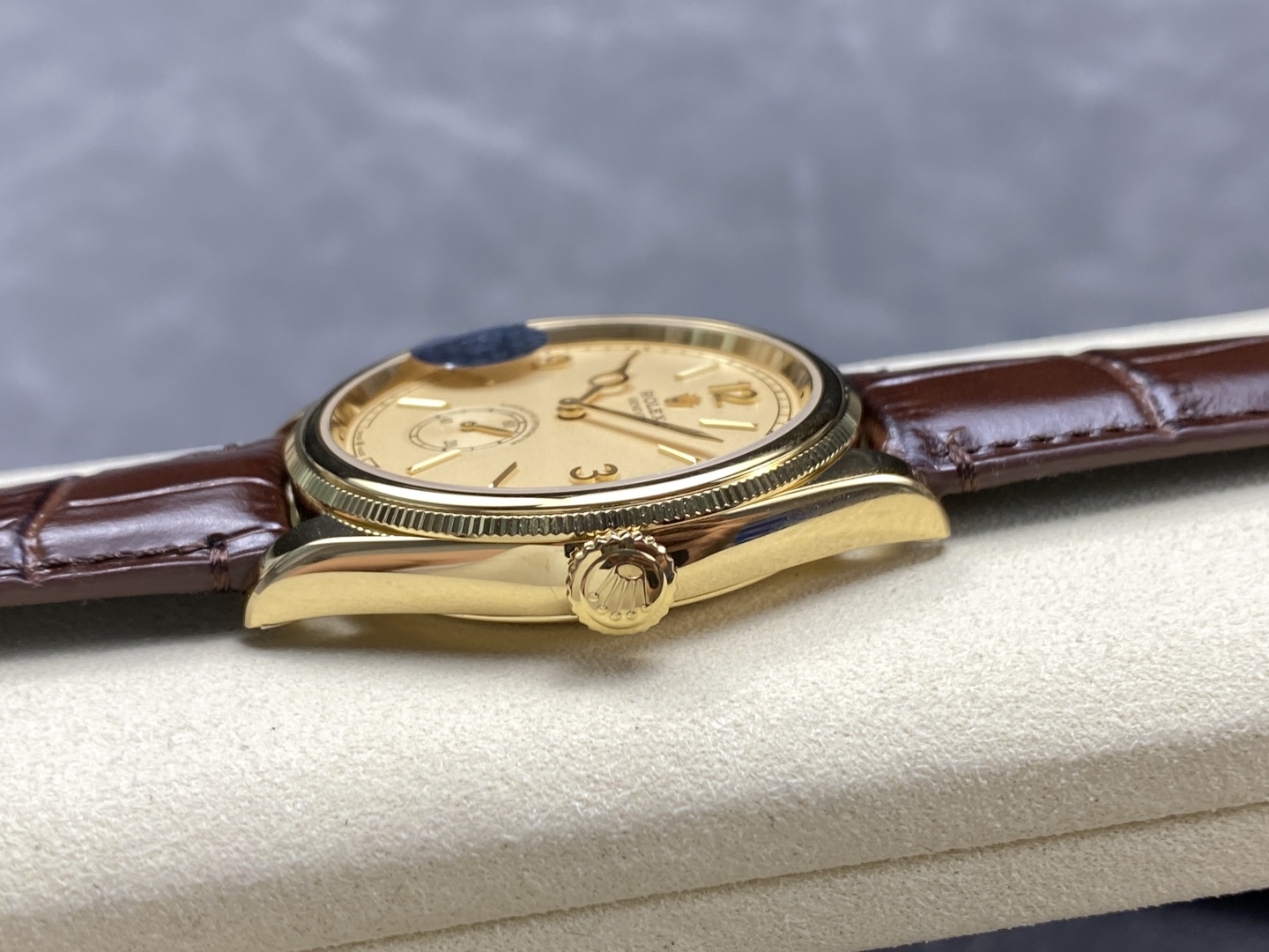 Seitliche Profilansicht einer Rolex 1908 Replik mit flachem goldfarbenem Gehäuse, geriffelter Lünette und braunem Lederband