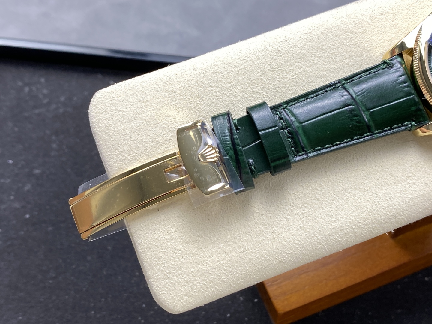 Close-up of dark green alligator pattern leather strap and gold Rolex crown clasp on cream display cushion