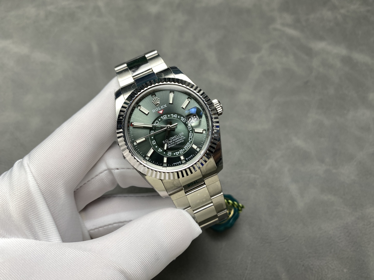 Rolex Sky-Dweller replica watch held with white gloves on a gray surface