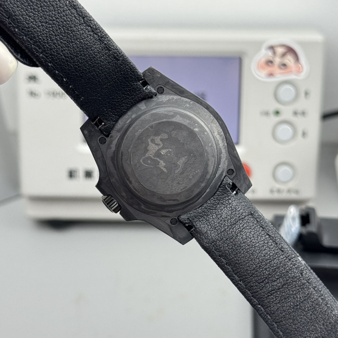 Back view of carbon fiber case Submariner replica watch showing worn metallic case back with screws, knurled crown, and black textured strap in workshop setting