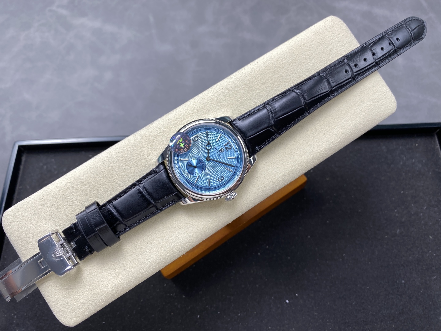 Elegant Rolex 1908 replica with vibrant blue guilloche dial, small seconds subdial, and black alligator leather strap resting on cream textured cushion