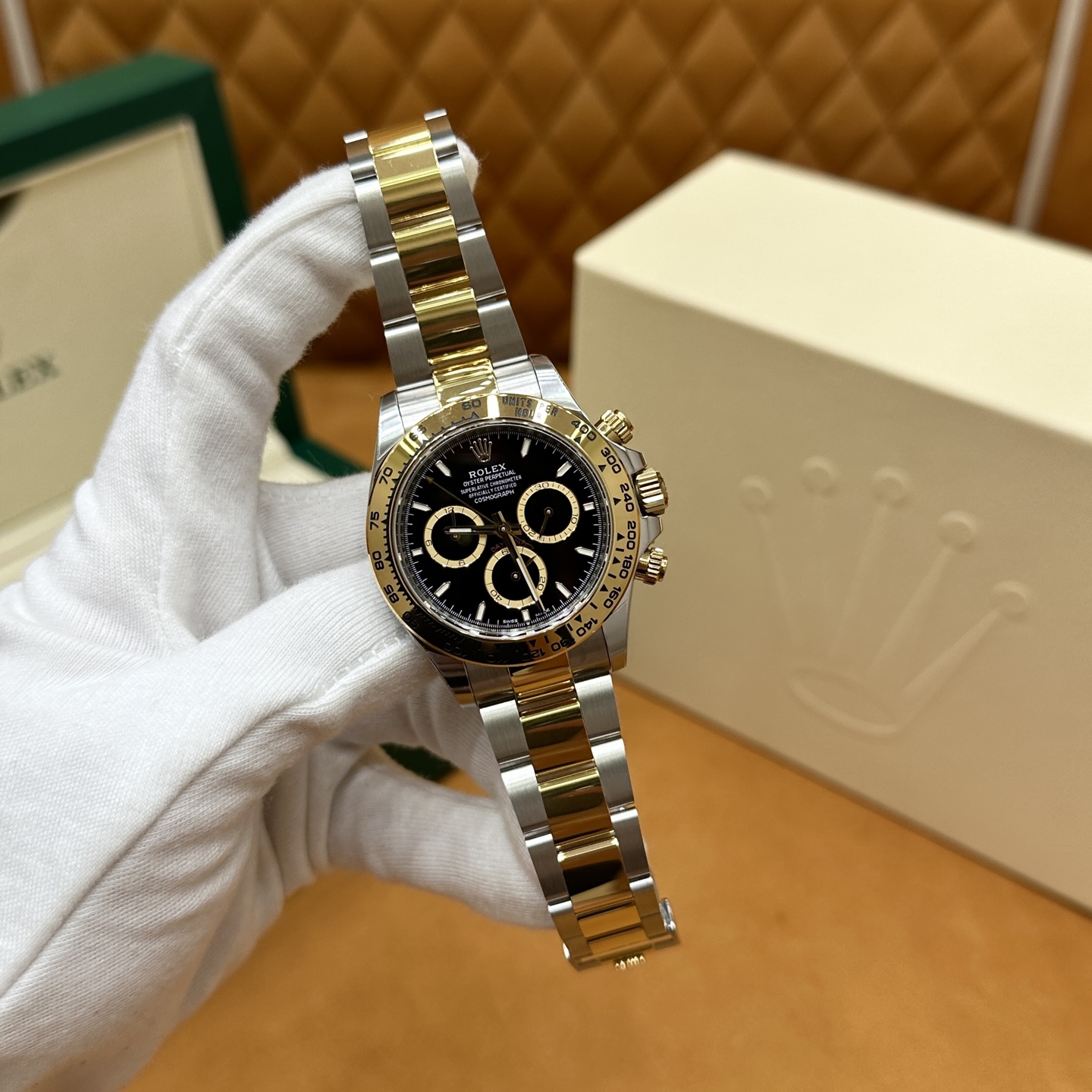 Two-tone Rolex Daytona replica with black dial and gold bezel on a gloved hand