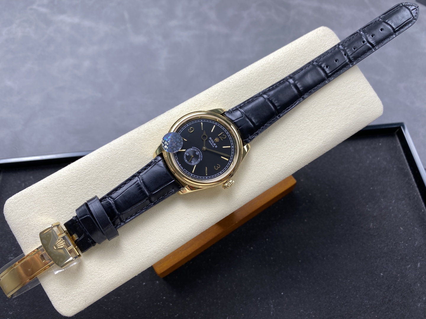 Gold Rolex replica watch with black leather strap displayed on a cream watch cushion