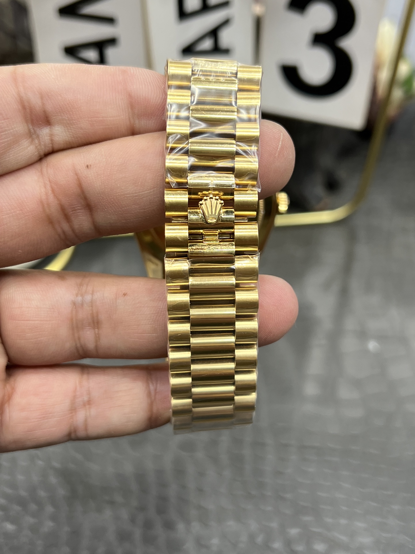 Close-up of the gold President bracelet on Rolex replica with embossed crown logo on clasp and protective film