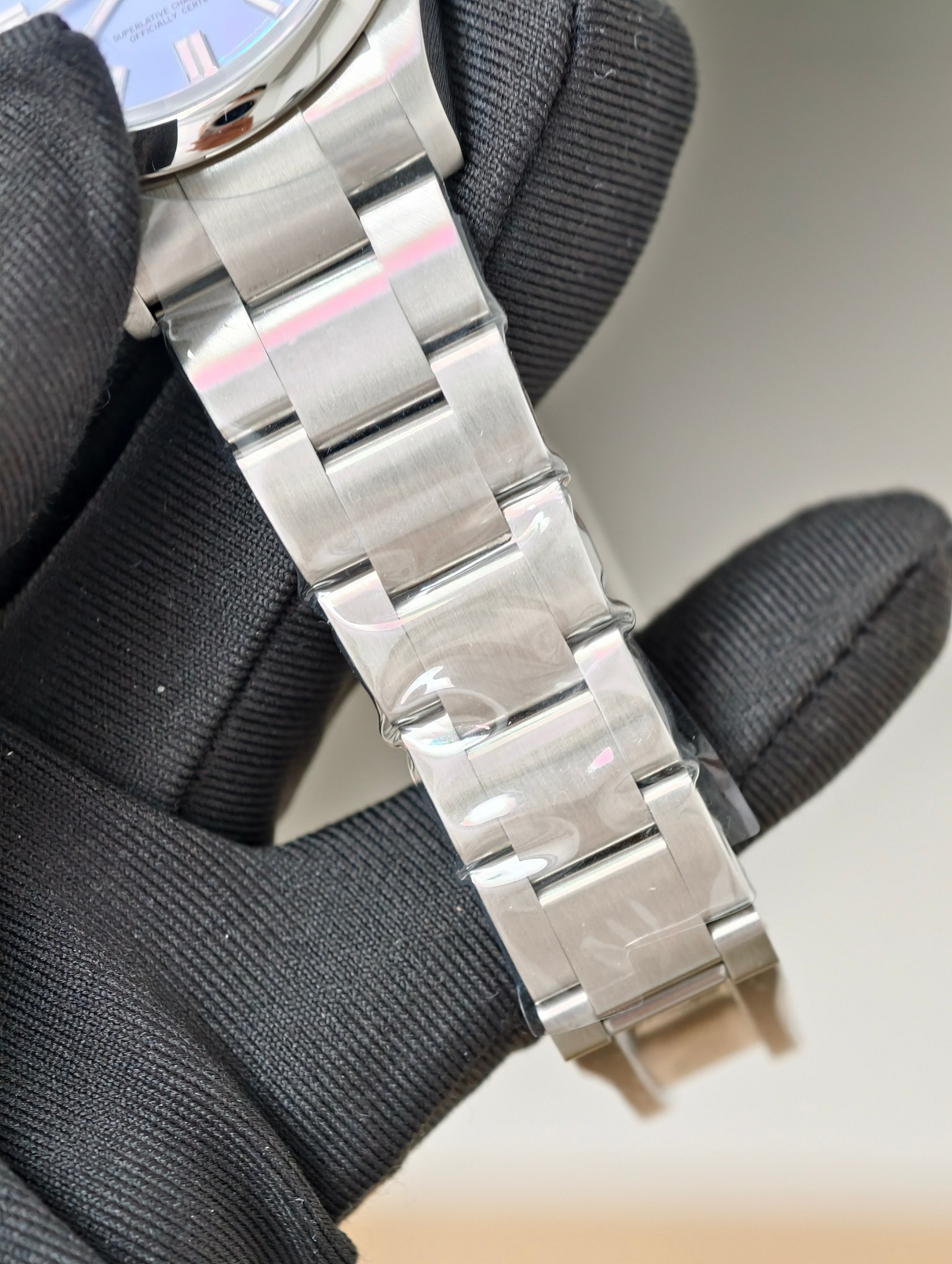 Oyster bracelet close-up with protective film and partial blue dial of Rolex replica