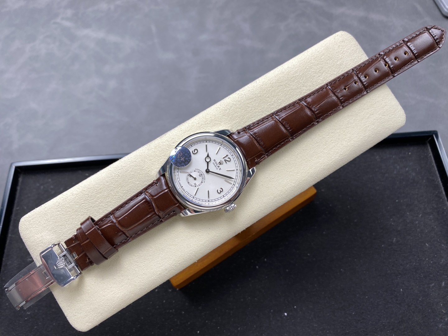 Replica Rolex 1908 con quadrante bianco, lunetta scanalata e cinturino in pelle marrone su cuscino di feltro crema