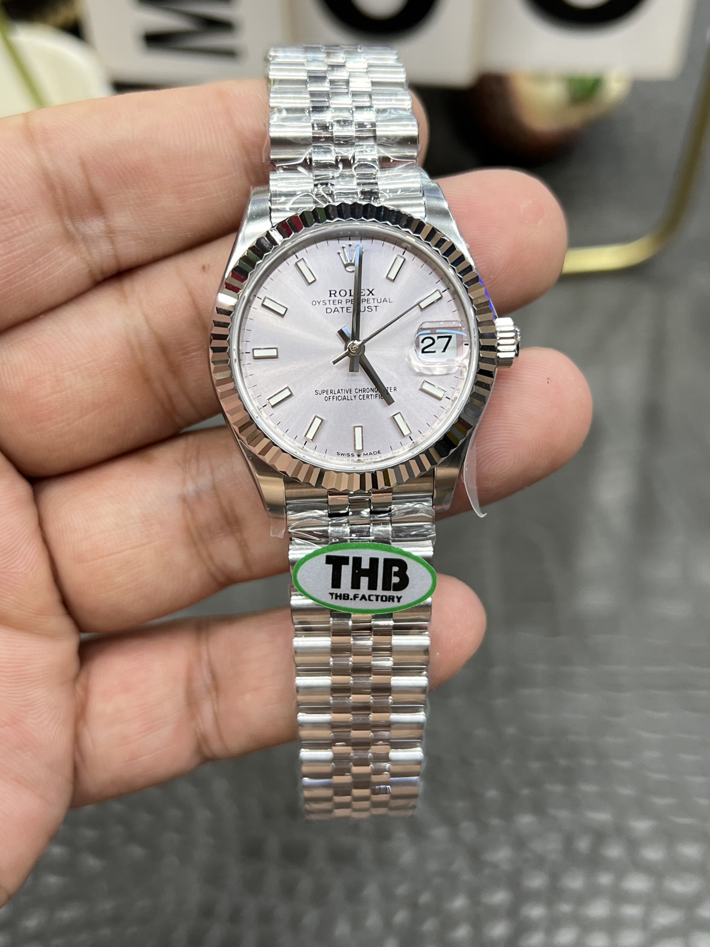خلفية ساعة رولكس مقلد مع غطاء أبيض وشعار تاج ذهبي وملصق THB