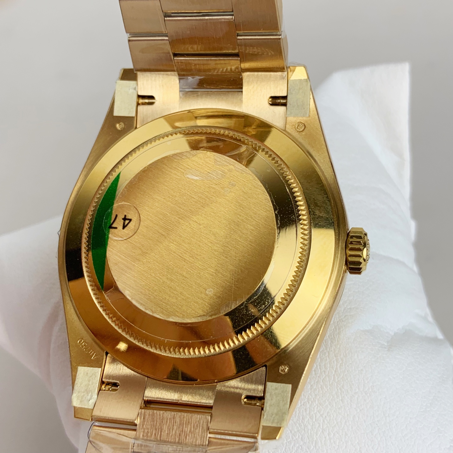 Back view of gold-colored watch caseback showing polished metal, brushed center disc, ridged screw-down bezel, small screws, and internal markings on white textured surface