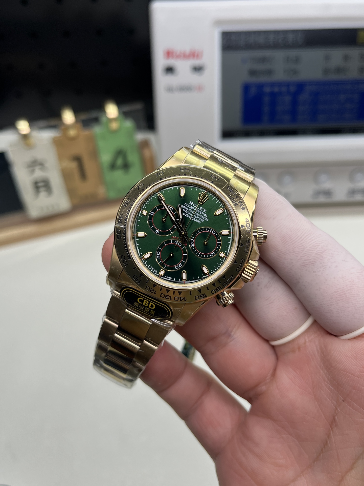 Rolex replica Daytona de oro con esfera verde y etiqueta CBD sobre un cronocomparador