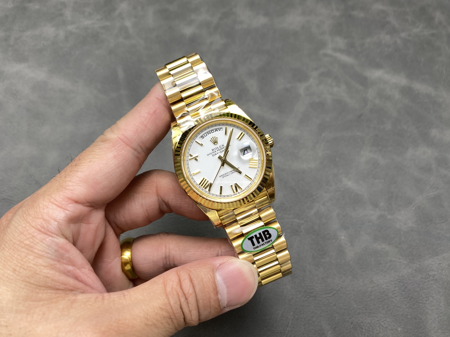 Gold Rolex Day-Date replica watch held in hand with white dial and President bracelet