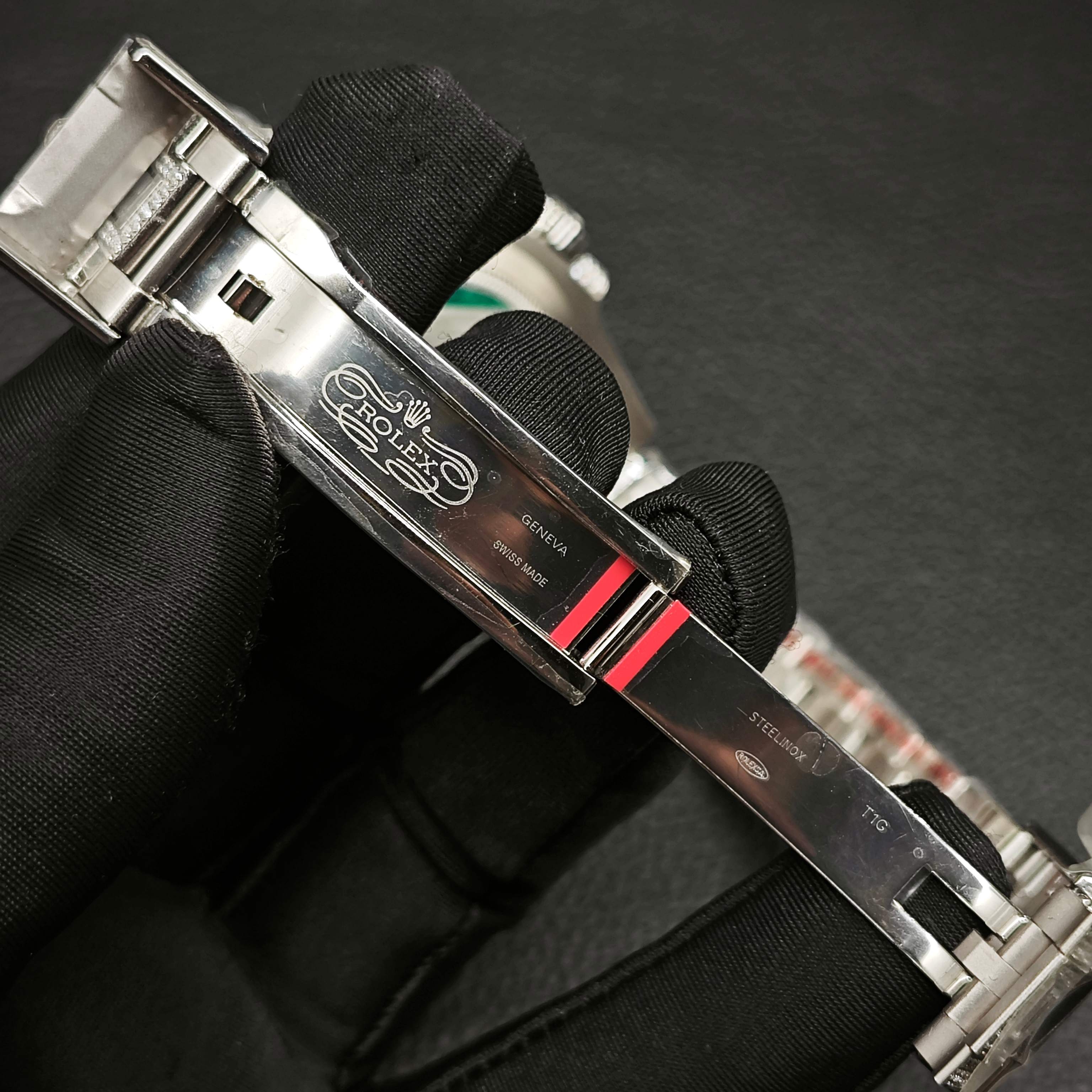 Rolex Submariner clasp with engravings held by gloved hands showing Swiss made quality markings